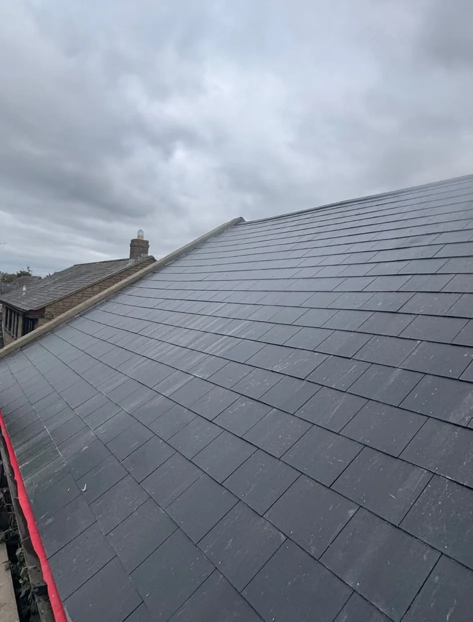 Completed new slate roof with ridge and neighbouring stone house, by CJroofing in Northumberland