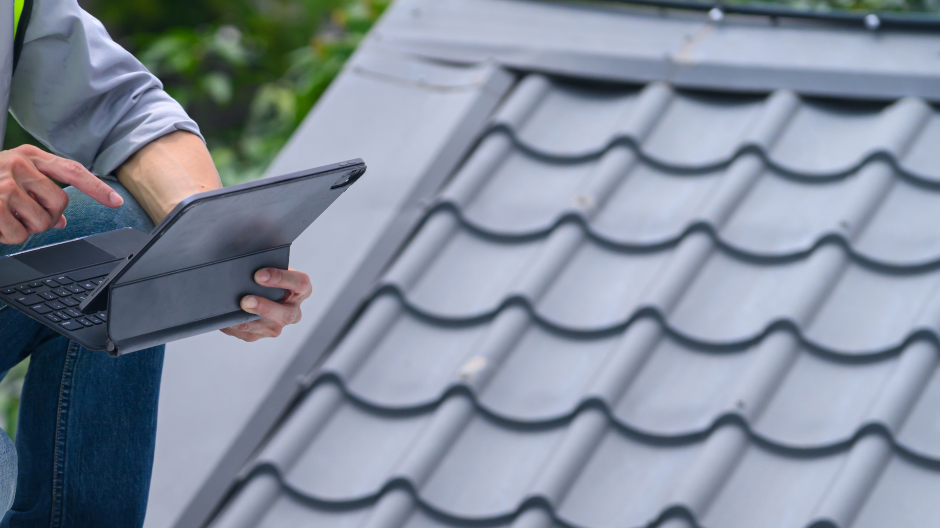 Roofer recording a roof inspection on a tablet beside a grey tiled roof