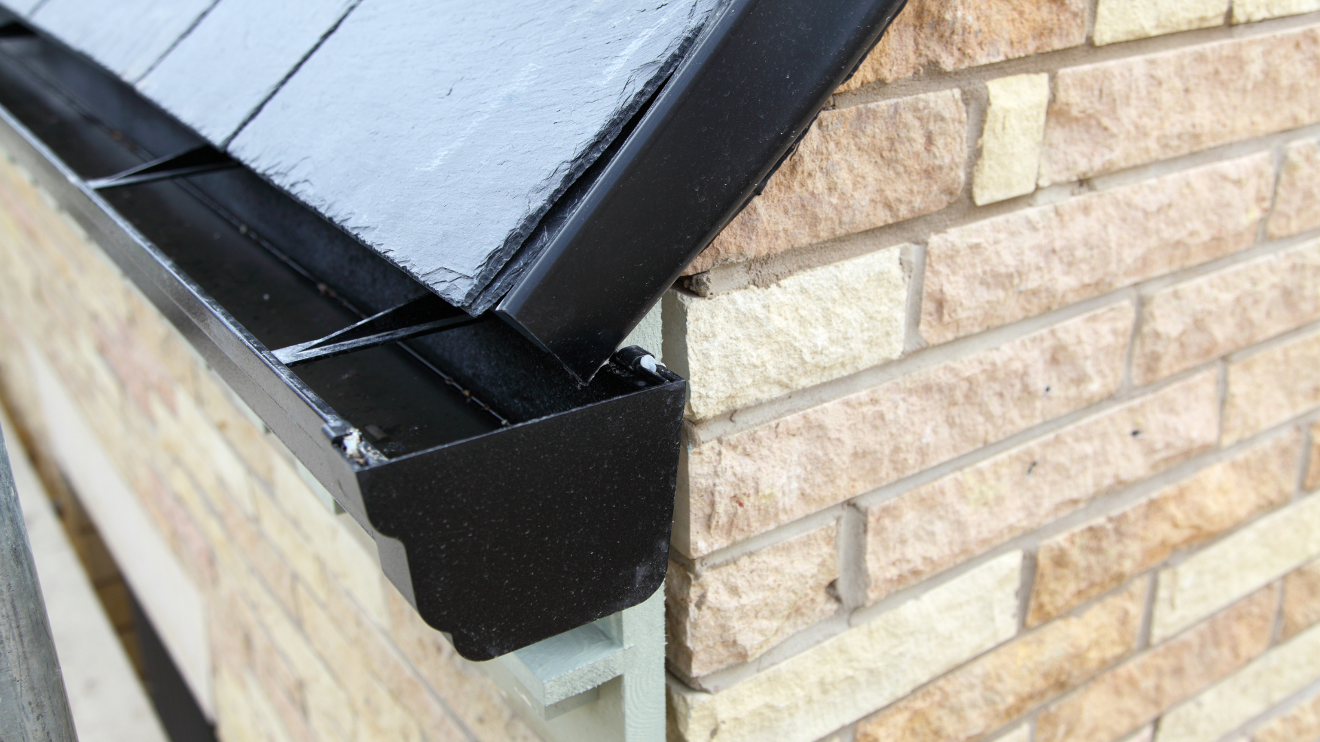 Black gutter and stop end fitted below a slate roof edge on a stone brick wall