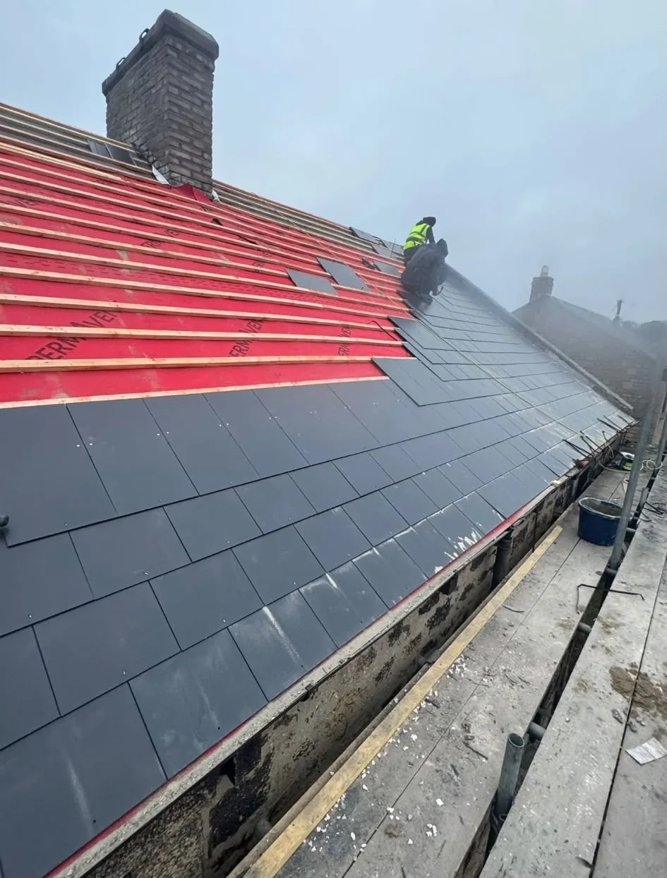 Roofers laying new slates over red breathable membrane and battens during a new roof installation