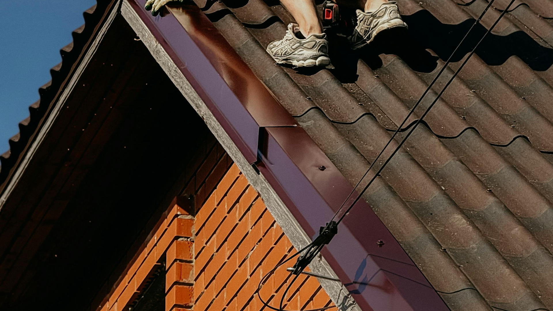 Roofer working on a tiled roof above a brick gable with new metal verge trim