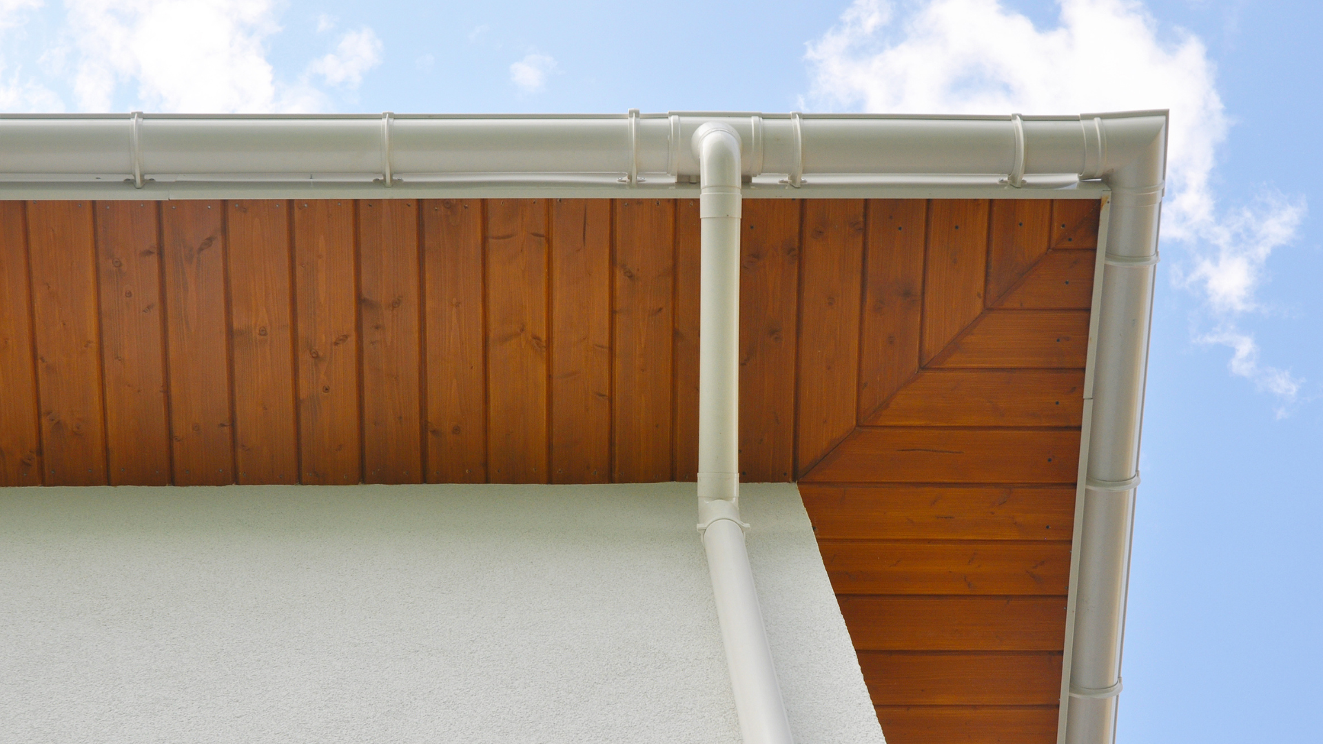Timber soffit boards with white guttering and downpipe under a roof overhang