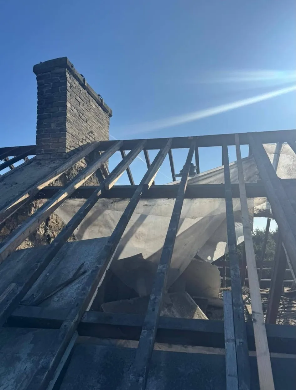 Roof stripped to bare rafters beside a brick chimney ahead of new roof installation
